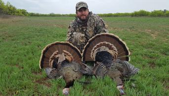 A man posing in front of two turkeys after hunting them